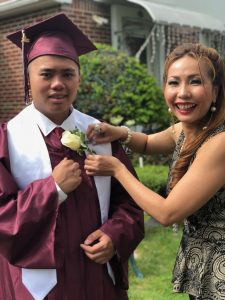 Woman pins flower onto young mans graduation gown.