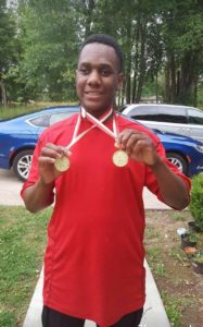 A smiling young man in a red shirt holding two medals